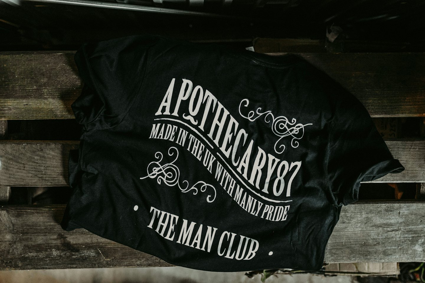 Zwart T-shirt met wit vintage design op een houten pallet.